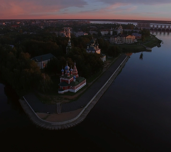 Вид с высоты птичьего полета на живописный городской пейзаж с рекой, мостом и церквями с куполами на закате.
