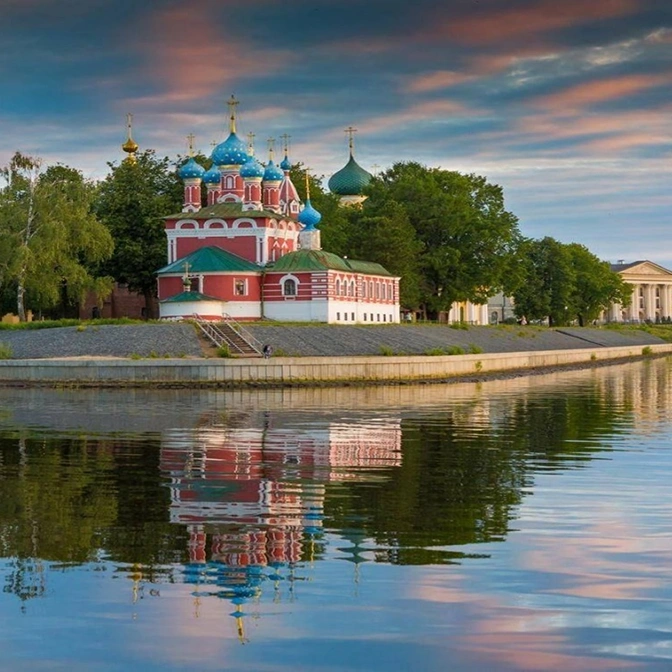 Советское здание с надписью Чайка на крыше, окруженное зелеными насаждениями и дорожками, на фоне голубого неба.